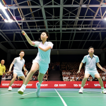 A dynamic action shot of badminton players competing in the All England Open Badminton Championships. Focus on speed and agility with the shuttlecock in mid-air. Include a diverse crowd of spectators in the background, showcasing the event's popularity.